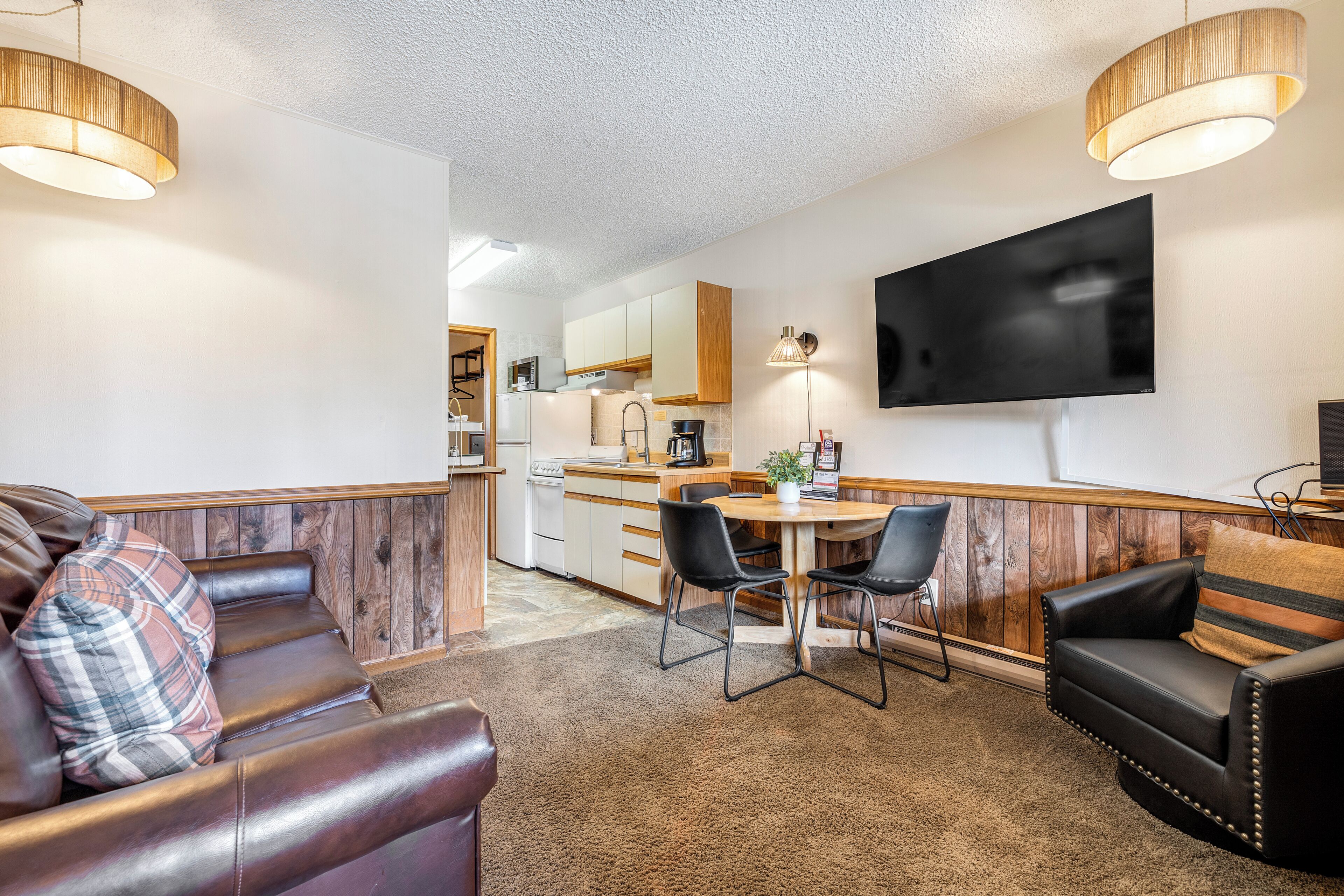 A compact living space with a kitchenette, a dining area, and a seating area with a TV mounted on the wall.