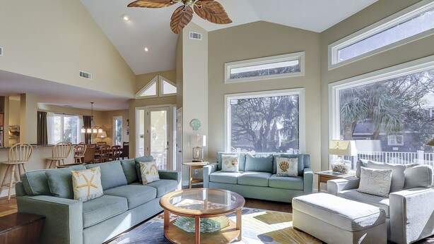 A spacious living room with a high ceiling, large windows, and a ceiling fan.
