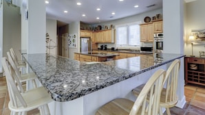 A spacious kitchen with granite countertops, wooden cabinets, and a central island with seating.