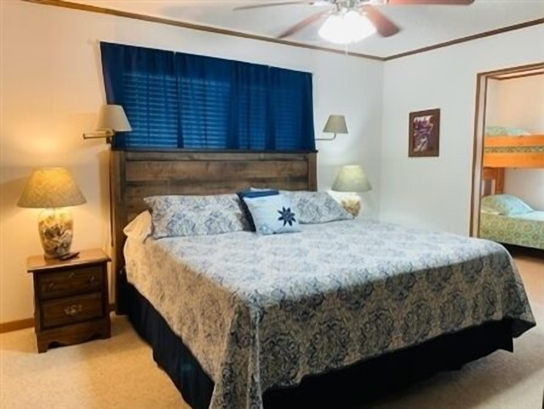 Une chambre à coucher comprenant un lit, deux lampes de chevet, un ventilateur de plafond, une table de chevet et une commode.