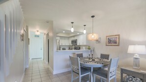 A dining area with a table and chairs, a kitchen in the background, and a hallway leading to a door. - LAKE PALMS 1 - Sanibel Condo Overlooking Lagoon (Sanibel)