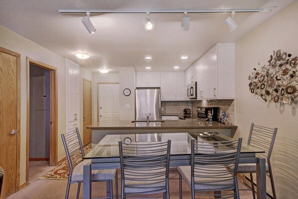A modern kitchen with a central island, stainless steel appliances, and a dining area with metal chairs.