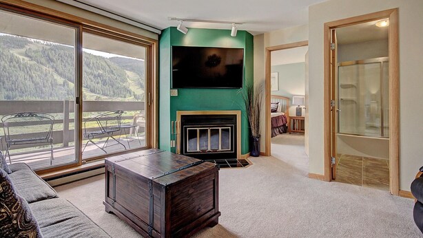 Un salon spacieux avec une cheminée, une grande télévision et un balcon offrant une vue sur les montagnes.