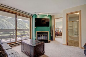 Un salon spacieux avec une cheminée, une grande télévision et un balcon offrant une vue sur les montagnes.