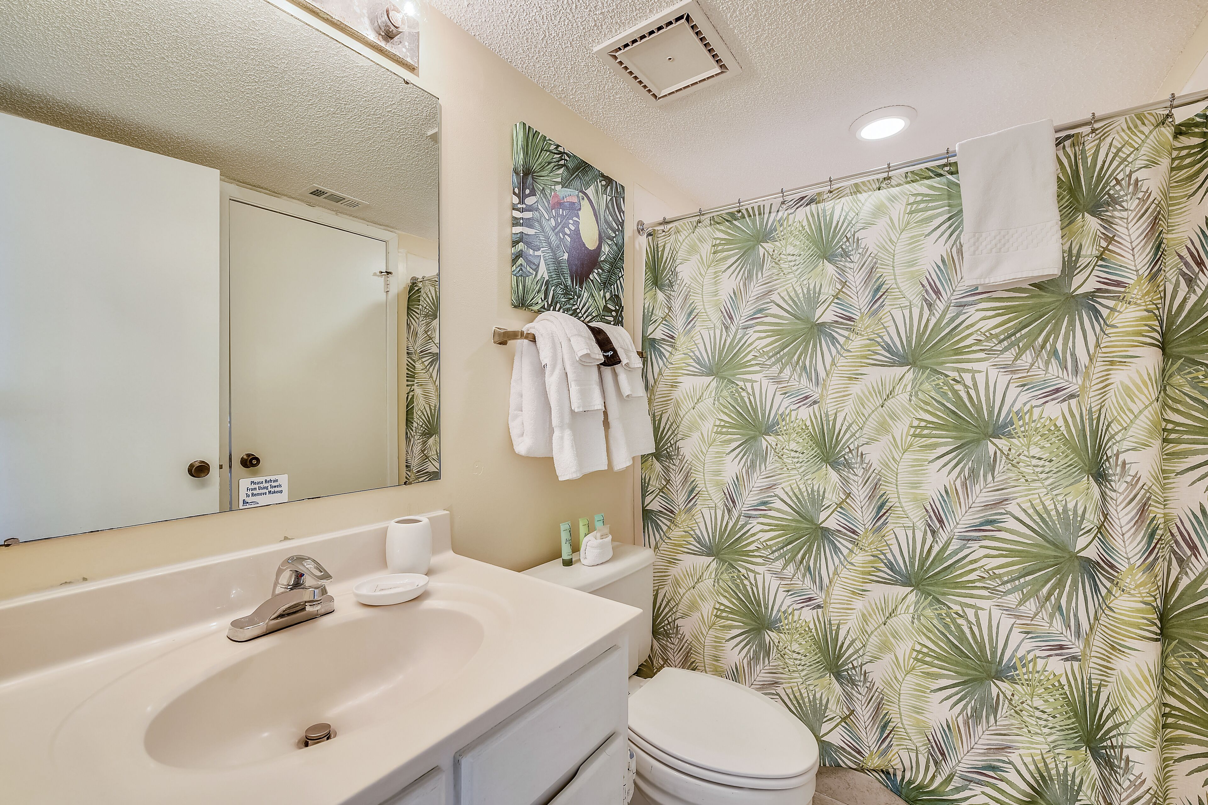 A bathroom with a white sink, a toilet, and a shower curtain with a tropical leaf pattern.