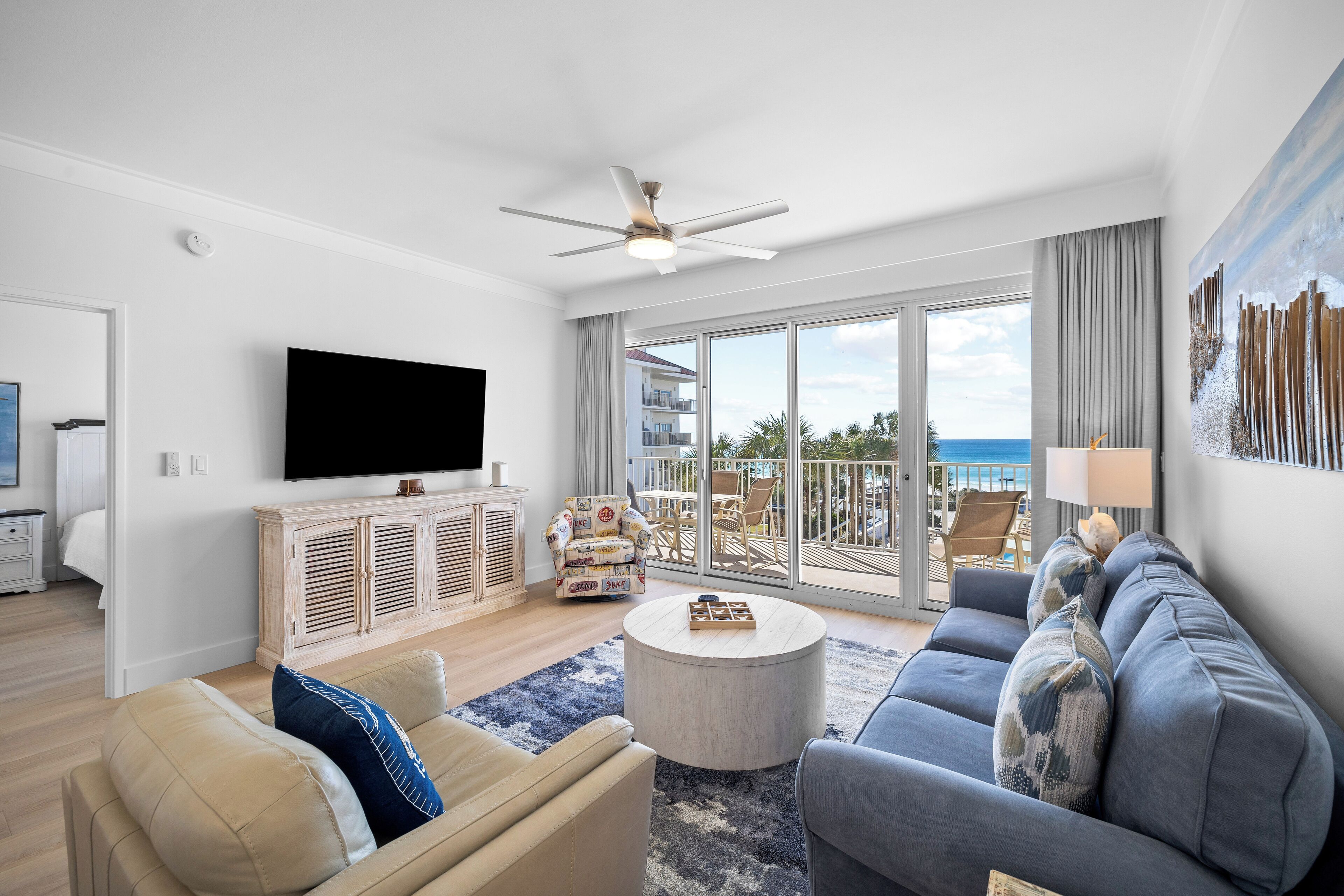 Een moderne woonkamer met een flatscreen-tv, een plafondventilator, een bank, een salontafel en een balkon met uitzicht op zee.
