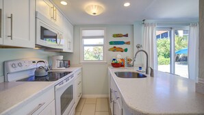 A compact kitchen with white cabinetry, a stove, a sink, and a window with a view of greenery outside.