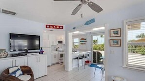 A modern kitchen with white cabinets, a large flat-screen TV, and a ceiling fan.