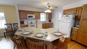 A modern kitchen with wooden cabinets, a central island, and a dining area with chairs and a table set for four.