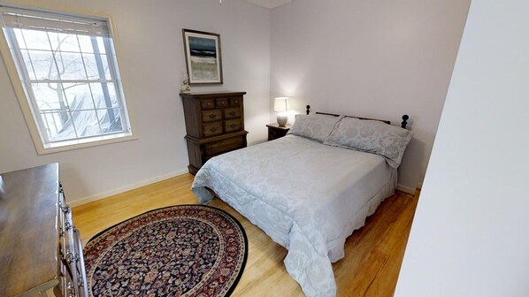 A bedroom with a bed, a nightstand, a dresser, a window, and a rug.