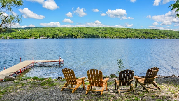 A lakeside view with wooden chairs and a dock extending into the water.