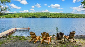 A lakeside view with wooden chairs and a dock extending into the water.
