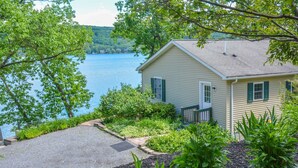 A house with a view of a lake, surrounded by greenery and a gravel driveway.