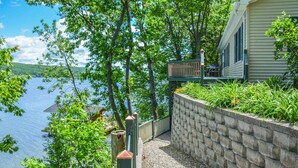 A lakeside cabin with a deck overlooking the water, a stone retaining wall, and a small garden area.