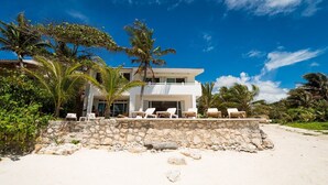 A beachfront property with a stone wall, lounge chairs, and palm trees. - Spacious Beachfront Living on Akumal Bay (South Akumal)