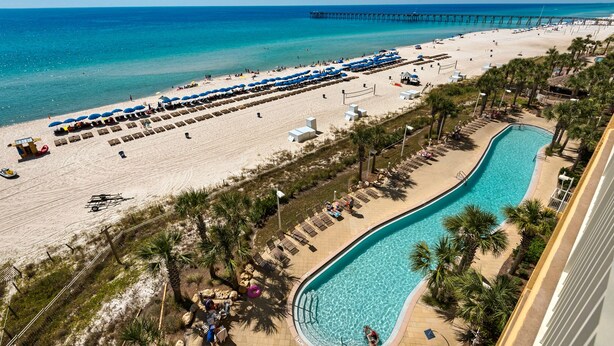 Ein Strandresort mit Schwimmbad, Strandsonnenstühlen und einem Pier im Hintergrund.