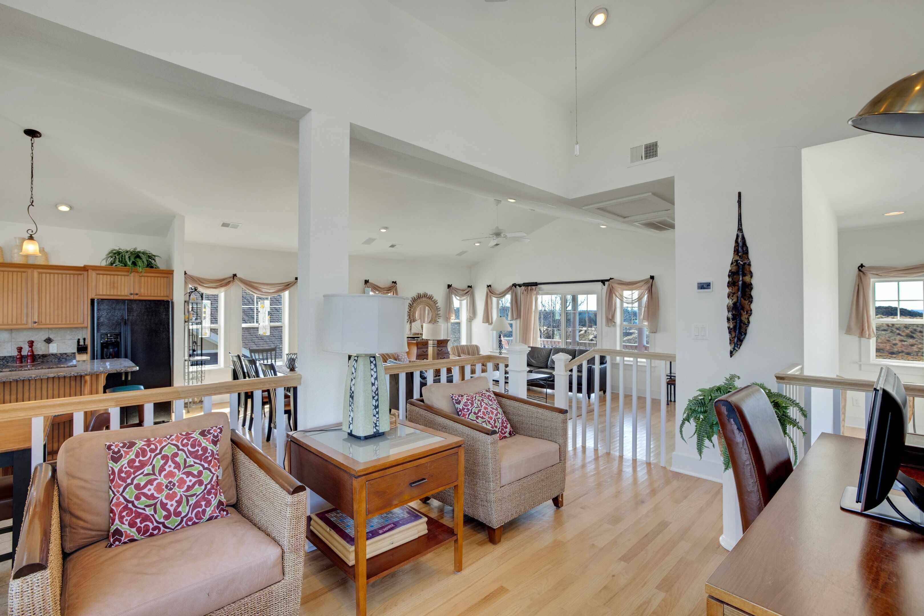 A spacious living area with a wooden dining table, two wicker armchairs, a side table, and a large window with curtains.