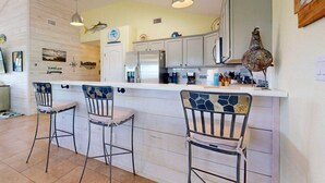 A kitchen with a white countertop, three bar stools, a refrigerator, and a decorative bird sculpture. - Parking for Boat, Shared Pool, Outdoor Seating Areas, Pet Friendly (Port Aransas)