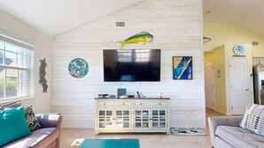 A living room with a television mounted on a white wooden wall, a cabinet below, and a sofa with cushions. - Parking for Boat, Shared Pool, Outdoor Seating Areas, Pet Friendly (Port Aransas)