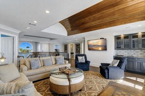 A spacious living room with a high ceiling, a large sofa set, a round coffee table, and a view to the outside. - 33 Dune Lane- Oceanfront & Beautiful! (Hilton Head Island)