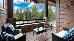 A wooden deck with wicker furniture, stone walls, and a view of trees.