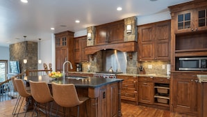 A spacious kitchen with wooden cabinets, a central island with bar stools, a stainless steel range hood, and a built-in microwave.