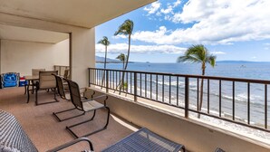 A balcony with a view of the ocean, palm trees, and a beach.