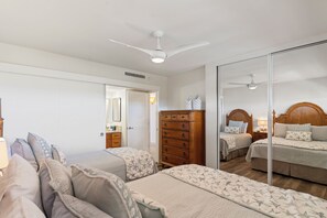 Une chambre avec deux lits, une commode en bois, un ventilateur de plafond et un miroir.