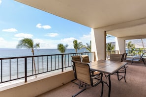 Ein Balkon mit Tisch und Stühlen, mit Blick auf den Ozean, Palmen und einem klaren Himmel.