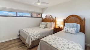 A bedroom with two beds, a ceiling fan, a nightstand with a lamp, and a window with a view of a bridge.