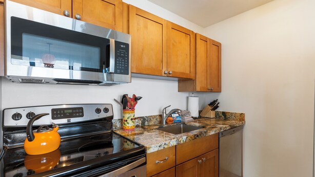 A kitchen with wooden cabinets, stainless steel appliances, a granite countertop, and a kettle.