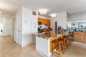 Una cocina moderna con una isla de granito, taburetes de madera y un ventanal amplio.