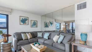 A modern living room with a grey sectional sofa, a wooden coffee table, and a large mirror reflecting the room.