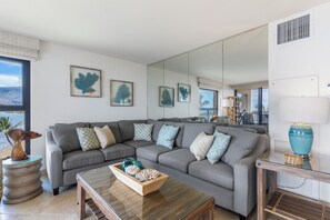 A modern living room with a grey sectional sofa, a wooden coffee table, and a large mirror reflecting the room.