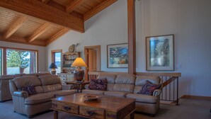 A spacious living room with a high ceiling and wooden beams, featuring a large sectional sofa, a wooden coffee table, and a staircase with a railing. - Bright lakeview home near Tahoe City, huge sunny lakeview deck (Tahoe City)