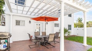 A patio with a table and chairs, an umbrella, and a grill. - Bikini Bottom | Charming Apt in Historic Home, Nearby Beach Access (Tybee Island)