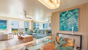 Un salon moderne avec une table basse en verre, un canapé et un grand tableau représentant de l’eau.