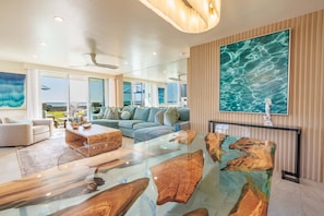 Una sala de estar moderna con una mesa de centro de vidrio, un sofá y un cuadro grande de un paisaje acuático.