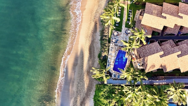 Vista aérea de un resort con playa, piscina y palmeras.