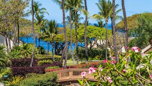 A tropical resort with palm trees, a wooden bridge, and a view of the ocean.