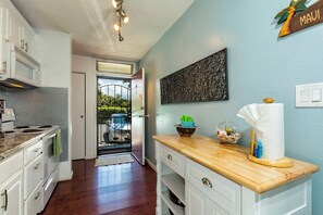 A kitchen with white cabinets, a wooden countertop, and a view to the outside.