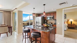 Quarto de hotel com cozinha, sala de jantar com mesa e cadeiras, e vista para o exterior.