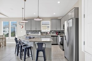 A modern kitchen with a large island, stainless steel appliances, and bar stools. - Coastal Cottage | Community Pools, Beach Access | Pet Friendly Escape (Gulf Shores)