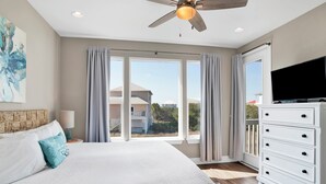 Een slaapkamer met een groot bed, een plafondventilator, een televisie en uitzicht op een balkon.