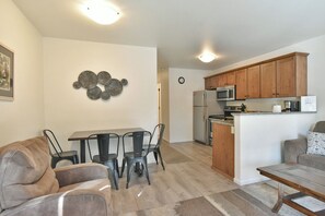 A modern kitchen with wooden cabinets, a stainless steel refrigerator, and a microwave. There is a dining area with a table and chairs.