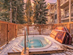 A hot tub on a wooden deck with a view of tall trees and a building in the background. - Wildwood Suites Bighorn Condo: Ski-in, Downtown Breck (Breckenridge)