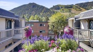 En bostadsbyggnad med en fasad av tegel, omgiven av färgstarka blomsterrabatter och med ett bergigt landskap i bakgrunden.