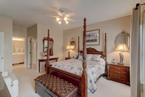 A four-poster bed with a canopy, a ceiling fan, bedside tables with lamps, a large mirror, and a view of a bathroom.