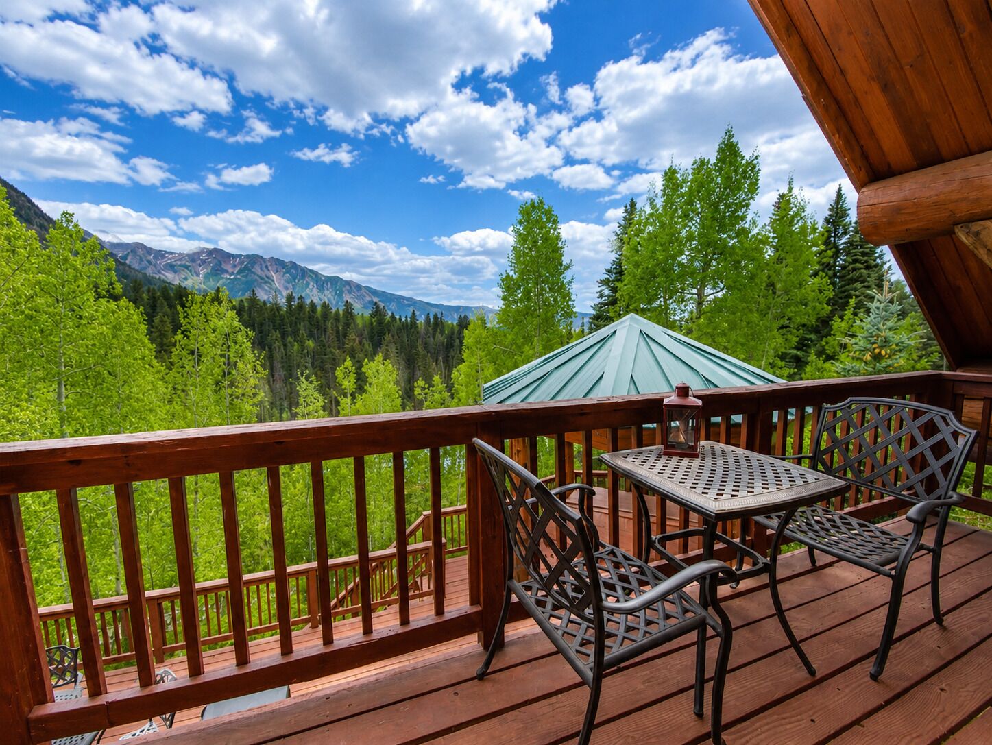 Une terrasse en bois avec une table et des chaises, offrant une vue sur une forêt et des montagnes.