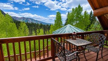 Une terrasse en bois avec une table et des chaises, offrant une vue sur une forêt et des montagnes.